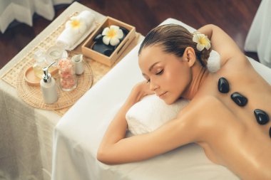 Lüks tatil köyündeki kaplıcalarda sıcak taş masajı. Gün ışığı sükunet ortamında, mutlu kadın müşteri bazalt taş masajından zevk alıyor. Rahatlatıcı bir sıcaklıkla vücudun üzerinde süzülüyor. Sessiz.