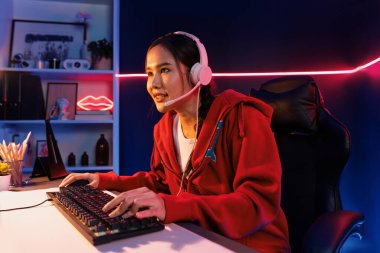 Güzel Asyalı kız flama kanalının sunucu kanalı çevrimiçi oyun odaklı kulaklık takıyor pastel renkli kulaklıklar takarak izleyicilerle çevrimiçi konuşuyor. Esport yetenekli takım oyuncuları neon mavi odada. Taktik.