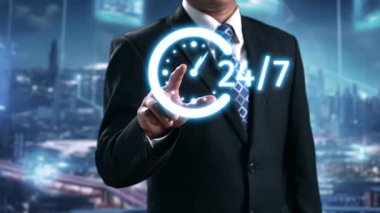 Resmi giyinmiş bir işadamı, dinamik ve modern bir iş ortamında 24 saatlik müşteri hizmetleri ve desteği simgeleyen dijital bir arkaplana güvenle karşı koyar. Dörtgen