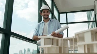 Gökdelen manzarasına bakarken yürüyen profesyonel mimar mühendisi. Masaya yerleştirilmiş ev modeliyle pencereye bakarken yetenekli proje yöneticisi proje planını tutuyor. Tasarım. İzleme