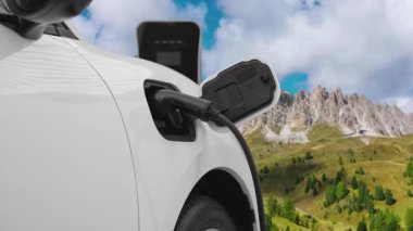 Temiz çevre için temiz enerjinin yol açtığı ilerici elektrikli araba kavramının arka planı olarak dağın tepesinde bulutun zaman kavramının yer aldığı doğal manzara. EV araba şarj istasyonunda şarj oluyor..