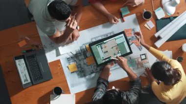 İnşaat mühendislerinin masa başında proje planıyla otururken tablet kullanarak ev yapısını dizayn etmelerine tepeden aşağı bir bakış açısı. Ekip planlama ve inşaat hakkındaki fikirlerin havadan görüşü. Sempozyum.