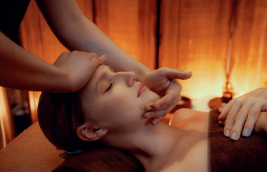 Beyaz kadın stres önleyici kafa masajı yapmaktan ve lüks otel veya otelde sıcak mum ışığında yüz güzelliği eğlencesi yapmaktan zevk alıyor. Sessiz.