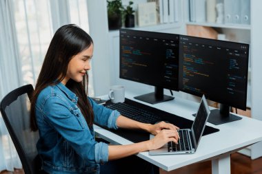 IT geliştiricisinde gülümseyen genç Asyalı dizüstü bilgisayarında kodlama programı verileriyle kotlu tişört giyerek çevrimiçi bilgi yazıyor. Güvenlik analizi iki ekran ile çevrili. Taktik.