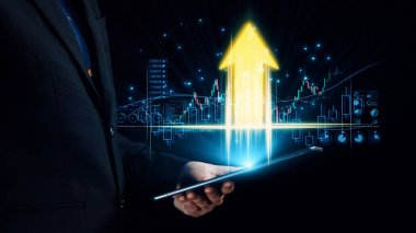 Takım elbiseli bir işadamı, yükselen finansal büyüme grafiği olan bir tablet tutuyor. Dijital analitik göstergeler başarı üzerine odaklanmış gelecekten gelen bir iş ortamı yaratıyor. Dörtgen