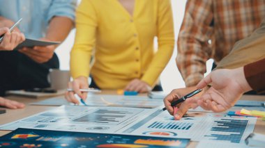 Modern bir ofiste takım çalışmasının dinamik bir sahnesi, stratejik bir iş toplantısı sırasında renkli çizelgeler ve grafikler üzerinde tartışan elleri gösteriyor. SACTR