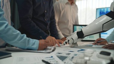 Robotik bir kolla çalışan, veri analizi ve yoğun bir masa üzerindeki görsel raporların sunumuna odaklanan insan profesyonelleri gösteren modern bir ofis sahnesi.
