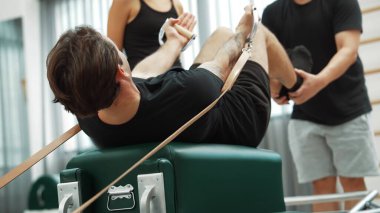 Müşteri, eğitmen desteğinin rehberliğinde kayışlarla Pilates reformatında egzersiz yapıyor. Sağlıklı bir adam pilates yapıyor ve üst vücut geliştirmek için Cadillac 'a asılıyor. Alışkanlık.
