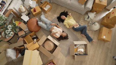 Oturma odasında yere uzanmış, mobilyaları etrafa saçılmış kız arkadaşın yukarıdan görünüşü. Lezbiyen aşıklar konuşurken tavana işaret ediyorlar. Myrmidon.