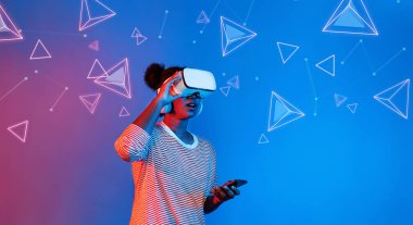 VR gözlüklü Afrikalı kız mavi ve pembe arka planda duruyor ve yüzen geometrik şekle bakıyor. Heyecanlı insan görsel gerçeklik dünyasına giriyor. Teknoloji yeniliği. Yaratıcılık.