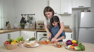 Zeki beyaz anne ve Asyalı kız birlikte yemek pişiriyor ve sebze doğruyor ya da akşam yemeği için salata hazırlıyor. Mutlu anne ve kız taze yemekle sağlıklı yemek yapıyorlar. Sağlıklı gıda konsepti. Pedagoji.