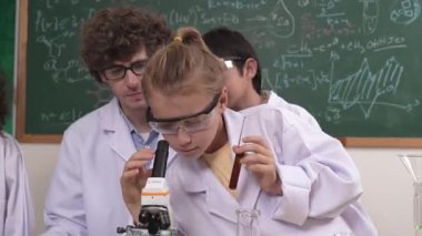 Kafkasyalı öğrenci kimyasal çözüm hazırlarken, yetenekli çocuklar mikroskop altında bakıyorlar. Profesyonel öğretmen, tahtada otururken deney yapıyor. Pedagoji.