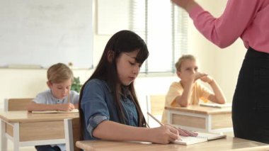 Asyalı mutlu öğrenci ilköğretim sınıfında soruları cevaplamak için gönüllü olurken öğretmen tahtaya cevap yazmak için öğrenciyi seçiyor. Sınıfta çeşitli çocuklar var. Pedagoji.