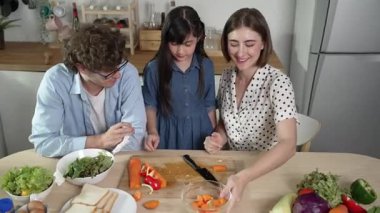 Çekici beyaz anne ve baba Asyalı kızıyla taze yemek pişirmek için birlikte vakit geçiriyorlar. Enerjik anne ve baba mutfakta salata yapmak için taze sebze hazırlıyor. Sağlıklı yiyecekler. Pedagoji.