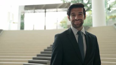 Akıllı iş adamı merdivenlerde kameraya bakıyor. İş elbisesi giyerken kameraya gülümseyen başarılı adamın yakın çekimi. Yönetici, kameraya bak. Hareket eden kamera. Sevinçli..