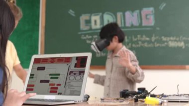 Kız kodlama sistemiyle uğraşırken metaworld 'e elektronik panoyla girmek için VR kulaklık takan bir çocuk. Çeşitli öğrencilerden oluşan bir grup program geliştirmek ve mühendislik kodu yazmak için birlikte çalışıyor. Pedagoji.