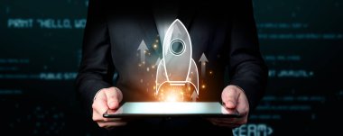 Elinde tablet tutan bir girişimci, başarı ve yenilik odaklı dijital bir ortamda yeni bir iş kurmayı simgeleyen fütürist bir roket grafiği sergiliyor. XDMCP