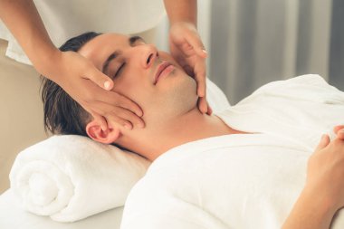 Beyaz adam stres önleyici kafa masajından ve lüks bir tatil beldesi veya otel spa salonundaki modern ışık ortamında yüz güzelliği eğlencelerini şımartmaktan hoşlanıyor. Sessiz.