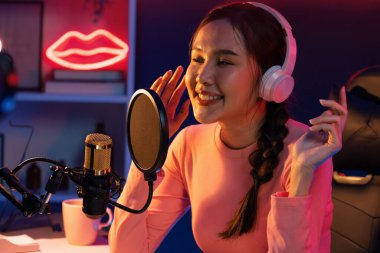 Genç ve güzel Asyalı yayıncının sunucu kanalı, dinleyicilerle sosyal medyada müzik dinliyor, pastel kulaklık takıyor, kapalı alanda neon ışıklı stüdyoda şarkı söylemek için mikrofon kullanıyor. Taktik.