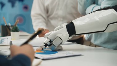 Bir robotik kol, modern ofis ortamlarında teknoloji ve yeniliğin bütünleşmesini, işbirliğini teşvik etmeyi sembolize eden bir iş toplantısı sırasında çizelgelerle etkileşir.