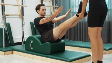 Erkek müşteri pilates ark fıçısında bacak kaldırma alıştırması yapıyor. Vücut dengesini, bacak dayanıklılığını ve spor salonundaki esnekliğini arttırmak için eğitmen yardımı ile birlikte. Öğrenci yalancı ve muziplik pozu veriyor. Alışkanlık.