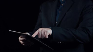 Takım elbiseli bir işadamı, maliyet azaltma grafikleri ve dijital simgeleri gösteren bir tablet tutarak, mali analiz ve stratejik yönetimi profesyonel bir bağlamda resmediyor. Dörtgen