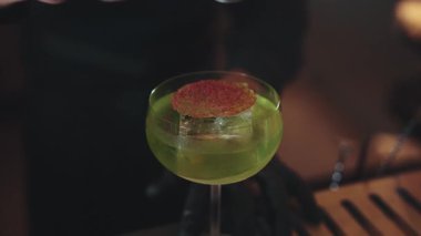 Yakın plan barmenin yeşil Midori Sour kokteyli ile karamelleştirilmiş turunçgil dilimli buzun üzerine tarçın gücü koyması lüks bar lüks sunumunda şık fincan tabağı kokteyli ikram etti. Vinosity.