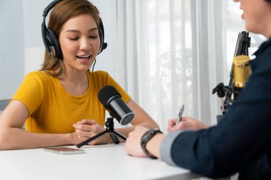 Gülümseyen radyo etkili sunucusu kulaklık takıyor kadın konuşmacı ile röportaj yapıyor sosyal medya internet sitesinden dinleyicilere bilgi paylaşıyor stüdyo kaydında sabah canlı yayın kanalı. İnfobahn.