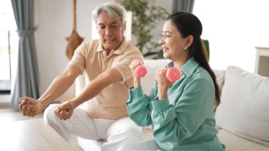 Mutlu yaşlı çift evde dambıllarıyla egzersiz yapıyor, kas gücü, eklem sağlığı ve sağlıklı yaşlanma için fiziksel sağlığa odaklanıyor. Emeklilik konsepti. Myrmidon.