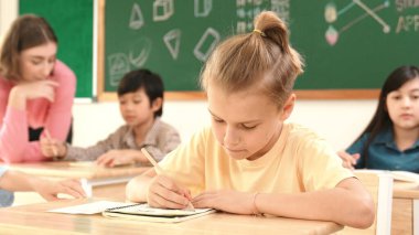 Stresli öğrenci, sınıfta çok kültürlü çocuklar yazarken ya da soruları cevaplarken tahtada otururken test yapmaya odaklanıyor. Becerikli öğretmen sınıf çalışmasını açıklıyor. Pedagoji.