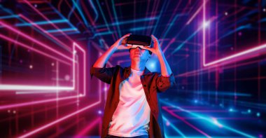 VR gözlüklü profesyonel erkek oyuncu parlayan neon ışıkla oyun oynuyor. Heyecanlı oyuncu artırılmış gerçeklik teknolojisi yeniliklerini kullanarak metaevrene bağlanmayı seviyor. Yaratıcılık.