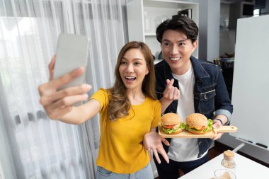 Gülümseyen sunucu şefler akıllı telefonla selfie çekerek sosyal medya kanalından canlı yayında yemek programında çift büyük hamburger yapıyorlar. İnfobahn.