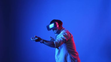 VR gözlüklü oyuncu sanal dünyaya girerken silah tutuşu yapıyor ve atış oyunu oynuyor. Mavi arka planda dururken simülasyon dünyasında zırh tutan yetenekli bir adam. Aygıt.