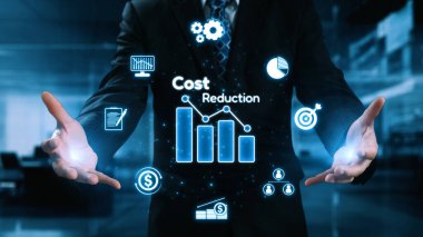 Bir işadamı modern bir ofiste maliyet azaltma stratejisi sergiliyor. Görsel unsurlar arasında, profesyonelliği vurgulayarak mali verimliliği ve yeniliği temsil eden grafikler ve simgeler yer alıyor. Dörtgen