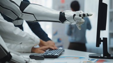 Bir robotik kol modern ofisteki bir bilgisayarla etkileşime girer, teknoloji ve yapay zeka gelişiminde yenilik ve işbirliği ruhunu somutlaştırır.