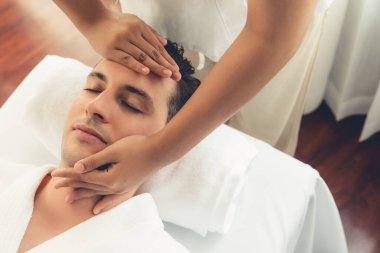 Beyaz adam stres önleyici kafa masajından ve lüks bir tatil beldesi veya otel spa salonundaki modern ışık ortamında yüz güzelliği eğlencelerini şımartmaktan hoşlanıyor. Sessiz.