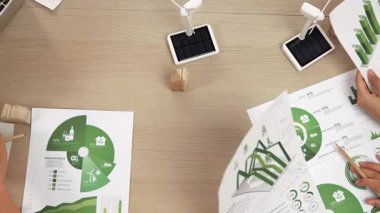 Eko evi projesini yel değirmeni tasarım modeli ve karbon ayak izini azaltmak için yeşil enerji kullanım grafiği ile toplantı masasında tartışan harika bir iş ekibi. Dünyayı kurtarın. Eline odaklan. Tanımlama.