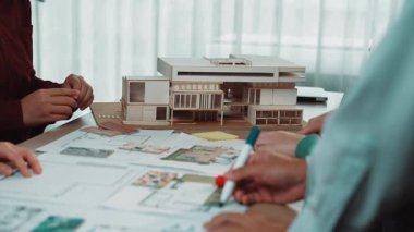 Bu görüntü dinamik bir mimari planlama oturumu yakalar, çizimler ve ölçekli bir model üzerine tartışmalara katılan elleri gösterir, takım çalışmasını ve yaratıcılığı vurgular. SACTR