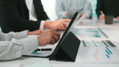 İşbirlikçi bir toplantıda yer alan profesyoneller, finansal veri ve grafikleri analiz etmek, takım çalışması ve modern iş stratejilerini eylem halinde göstermek için dijital tabletler kullanıyorlar. SACTR