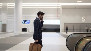 Profesyonel lider yürüyen merdivene doğru yürürken iş ekibini başlangıç projesi için arıyor. Akıllı iş adamı telefon kullanarak pazarlama planından iş arkadaşına bahsediyor. İş ekibi. Sevinçli..