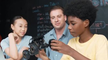 Afrikalı çocuk araba modelini dizüstü bilgisayar ve kabloyla incelerken öğretmen de karatahtadaki robotik yapıyı şifreli ya da STEM sınıfında hızlı bir şekilde açıklıyor. Eğitim. Öğretim