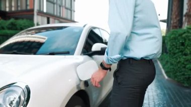 İlerici işadamı, şehir merkezinde dolaşmadan önce şarj cihazından elektrikli arabasına şarj prizi takıyor. Çevre dostu şarj edilebilir araba, sürdürülebilir ve temiz enerjiyle çalışıyor..