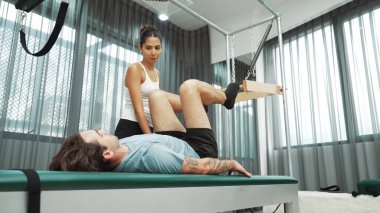 Cadillac ekipmanları üzerinde bacak kaldırma egzersizinde müşteriye yardımcı olan yetenekli pilates eğitmeni. Kadın antrenör, Cadillac 'ın bacak gerdirme hareketine yardım ediyor. Temel bağlantıyı geliştirmek için, bacak esnekliği için. Alışkanlık.