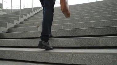Akıllı bir iş adamının elinde çantayla merdivenlerden yukarı çıkışının en üst görüntüsü. Profesyonel proje yöneticisi merdivenlerden çıkıp işyerine gidiyor. Yeteneklerini arttırmak, terfi almak, seyahat etmek. Sevinçli..