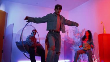 Çok kültürlü bir arkadaş kürsüde otururken Asyalı yetenekli bir dansçı modern müziğe geçiyor. Profesyonel dansçı, hipster takımı tezahürat yaparken ve desteklerken enerjik adımlar atıyor. Mutluluk.