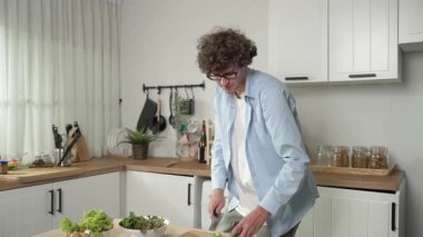 Mutlu baba yemek pişirirken müziğe geçiyor ve modern mutfakta öğle yemeği hazırlıyor. Aktif baba, sebze ve mutfak gereçleri ile çevrili sağlıklı yemek ya da salata yaparken şarkıyla dans ediyor. Pedagoji.