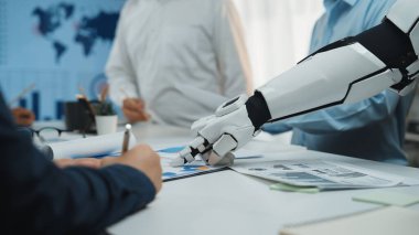 Bir robotik el, bir iş görüşmesi sırasında belgelerle etkileşime girer. Teknoloji ve işbirliğinin modern işyerlerinde giderek artan bütünleşmesini sembolize eder. Noogenesis