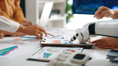 Modern bir iş ortamında insan eli ve veri tabloları üzerinde işbirliği yapan bir robot kolu, teknoloji ve profesyoneller arasındaki karar verme mekanizmasını vurguluyor.