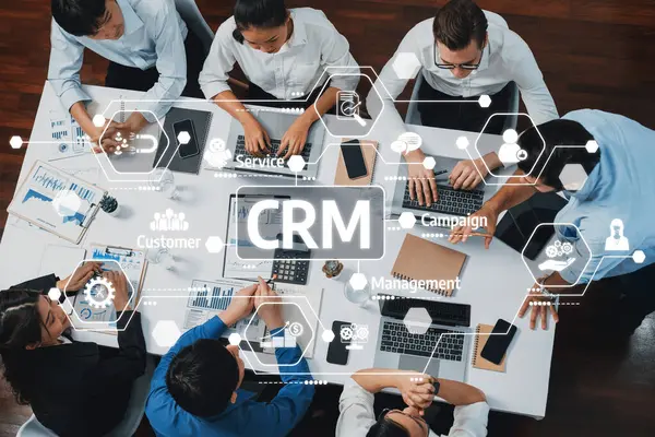 Modern ofis ortamında dijital arayüzler ve analitik araçlarla çevrili CRM sistem geliştirme üzerinde çalışan bir iş ekibinin tepeden tırnağa görüntüsü. Dostluk
