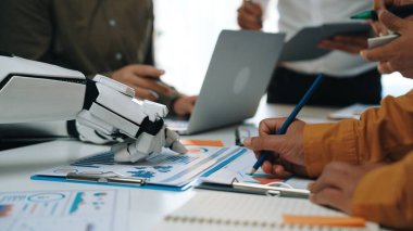 Bir iş toplantısına yardım eden robotik bir kol, işbirliği, veri analizi ve teknolojinin profesyonel ortamlara entegrasyonunun yer aldığı modern bir ofis sahnesi. Noogenesis